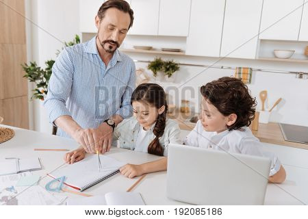 Clear explanation. Loving little schoolchildren listening attentively to their young father explaining geometry and inscribing a circle with a pair of compasses