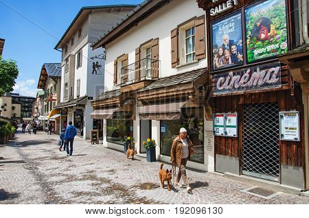 Megève, France - June 25, 2016. View of street with shop, cinema and madam with dog in Megève, a famous ski resort located in Haute-Savoie Province, near the Mont Blanc in the French Alps