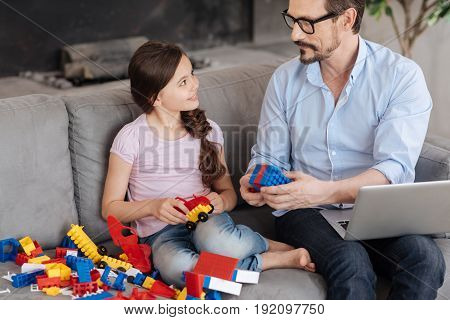 Symbol of togetherness. Handsome young father sitting on the sofa next to his daughter and showing her how two pieces of erector set match