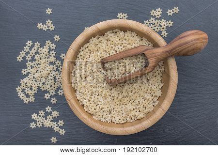 Star Shaped Noodles In A Wooden Bowl And Olive Wood Scoop On Black Background Of Slate Or Stone