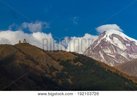 Ancient Trinity Church And A Snow Capped Mountain Of Kazbegi