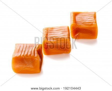 three toffee caramel candies in row close-up isolated on white background