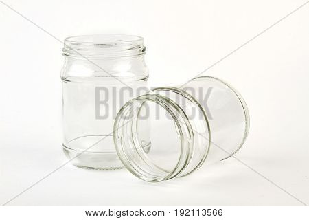 Two glass jars, white background. Couple of clear jars, one fell.