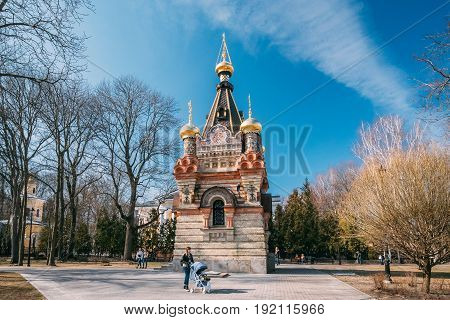 Gomel, Belarus - March 8, 2017:  Young Woman With A Stroller Walking In City Park At Sunny Spring Day. Famous Local Landmark Is Chapel-tomb Of Paskevich On Background