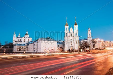 Vitebsk, Belarus - February 15, 2017: Traffic At Lenina Street And Landmarks On Background. Holy Assumption Cathedral, Holy Resurrection Church And City Hall In Evening Or Night Illumination At Winter