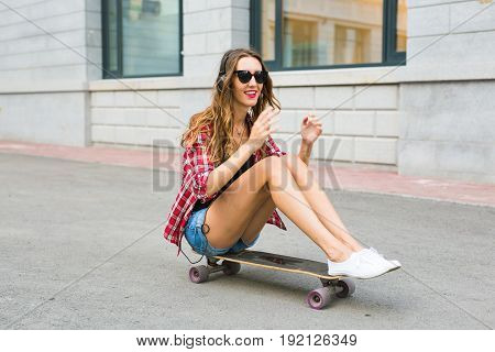 Young woman sitting on the skater. Smiling woman with skateboard in outdoors.