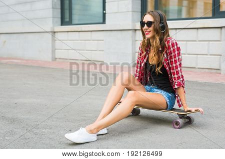 Young woman sitting on the skater. Smiling woman with skateboard in outdoors.