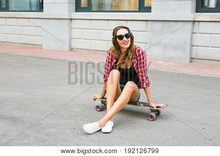 Young woman sitting on the skater. Smiling woman with skateboard in outdoors.
