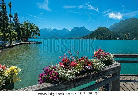 Pier with flowers on the lake of Annecy, in the village of Talloires. Mountains landscape and blue sky on background. France