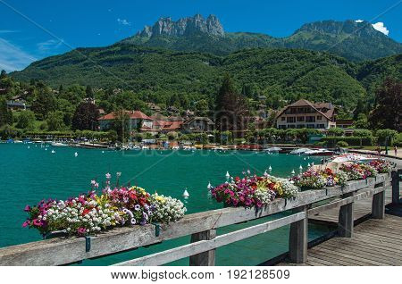 Pier with flowers on the lake of Annecy, in the village of Talloires. Mountains landscape, village and blue sky on background. France
