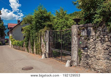 Street and closed gate in the village of Talloires, next to the Lake of Annecy. Mountains landscape and blue sky on background. France