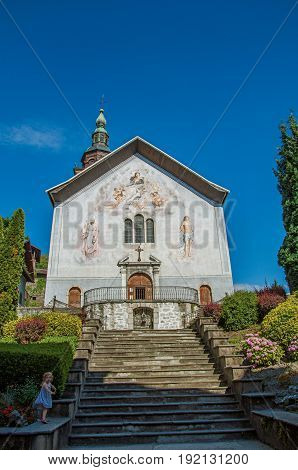 Conflans, France - June 29, 2016. Church with steeple, paintings and child in city center of Conflans, a medieval hamlet in Haute-Savoie department, Auvergne-Rhône-Alpes region, south-eastern France