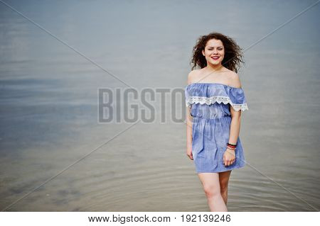 Portrait Of A Beautiful Girl With Curly Hair Wearing Marine Blye Dress Stands In The Water.