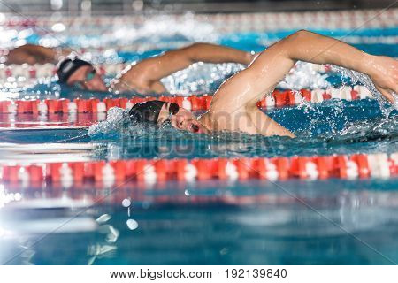 Side view of three male swimmers doing free style in different swimming lanes
