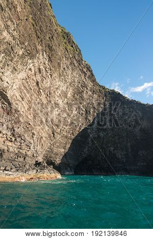 Cave entrance in rocky shore of Na Pali coastline from sunset cruise boat trip