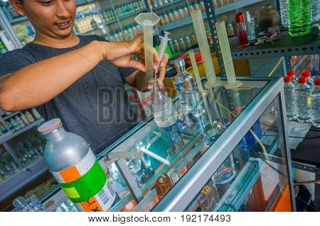 BALI, INDONESIA - MARCH 08, 2017: Unidentified man using syringes and pipettes mixing essences to prepare perfumes for the perfume store in Denpasar Indonesia.