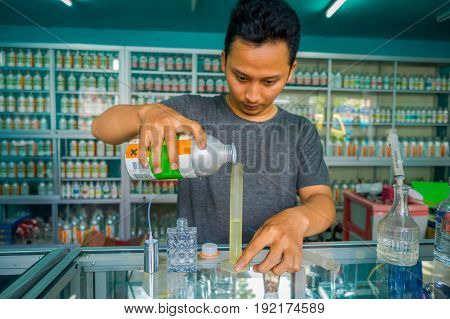 BALI, INDONESIA - MARCH 08, 2017: Unidentified man using syringes and pipettes mixing essences to prepare perfumes for the perfume store in Denpasar Indonesia.