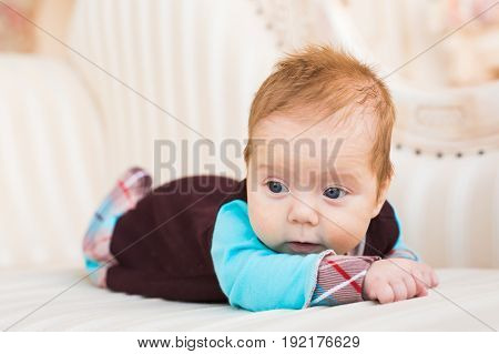 Adorable baby boy with red hair and blue eyes. Newborn child lyling in couch