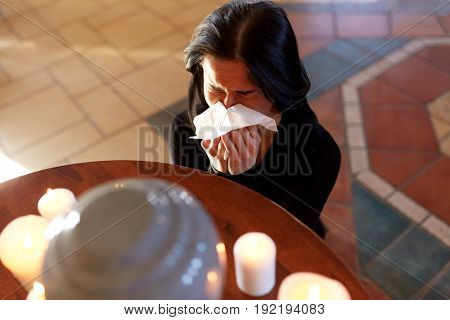 cremation, people and mourning concept - woman with wipe and cinerary urn crying at funeral in church
