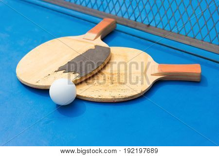 old pingpong rackets and ball and net on a blue pingpong table