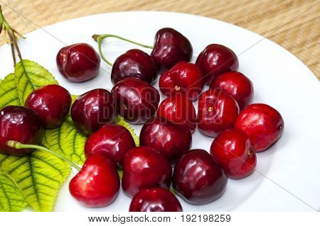ripe cherry on a white plate with green leaves