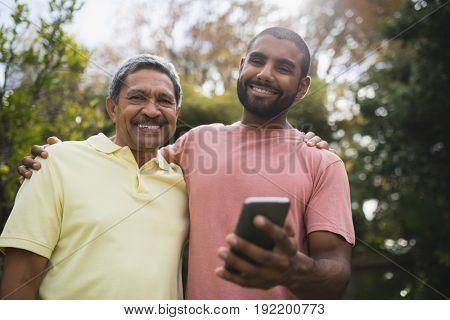 Low angle view of smiling father and son with mobile phone at prk
