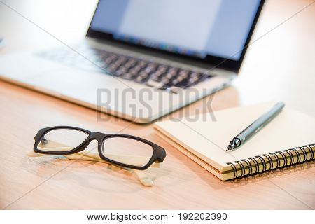 Glasses binder notebook pen and laptop on wooden office desk use for background in business management and learn education concepts