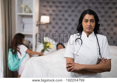 Portrait of serious nurse standing with patient on bed at home