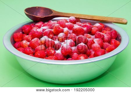 Strawberries from the manufacturer with sugar and jars for making jam on a green background.