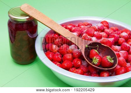 Strawberries from the manufacturer with sugar and jars for making jam on a green background.