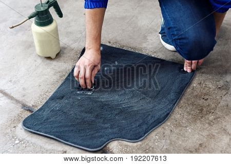 Details of automobile cleaning - male using professional chemical solutions to clean car floor mats.