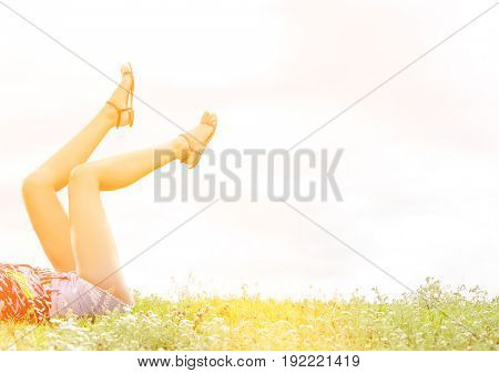 Low section of woman with feet up lying on grass against sky