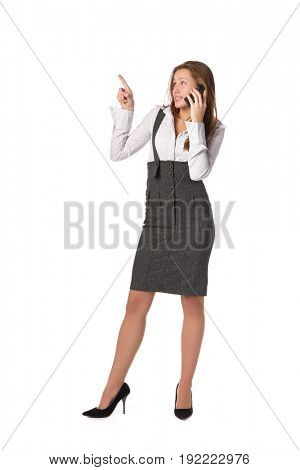 The young woman talks by a mobile phone and shows on an imaginery object over white background.