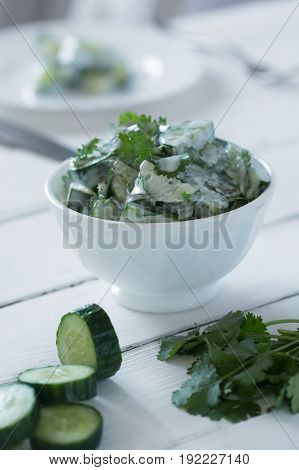 Cucumber salad with coriander and yogurt dressing on the white wooden background