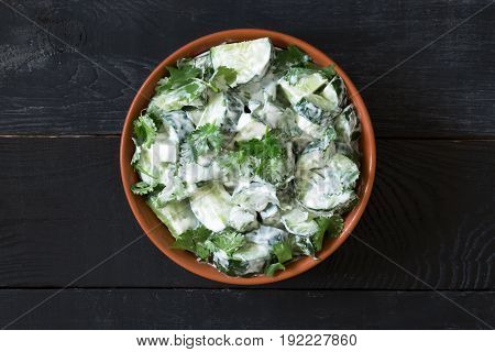 Cucumber salad with coriander and yogurt dressing on the black wooden background