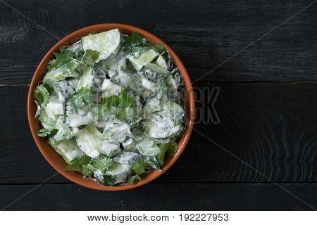Cucumber salad with coriander and yogurt dressing on the black wooden background