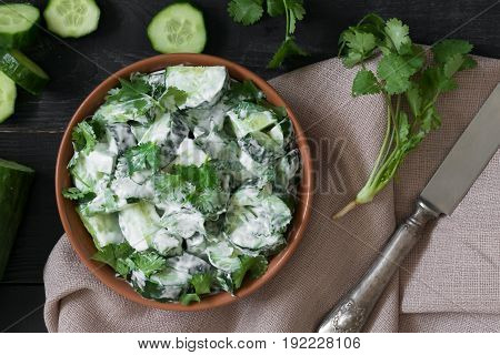 Cucumber salad with coriander and yogurt dressing on the black wooden background
