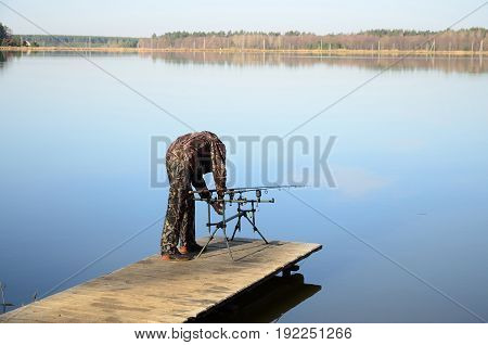 The fisherman installs two feeders on a rod pod with electronic bite alarms on a pier by lake