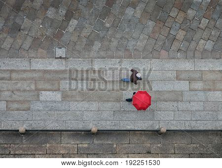 A view of walking people from above. One of them is with red umbrella.