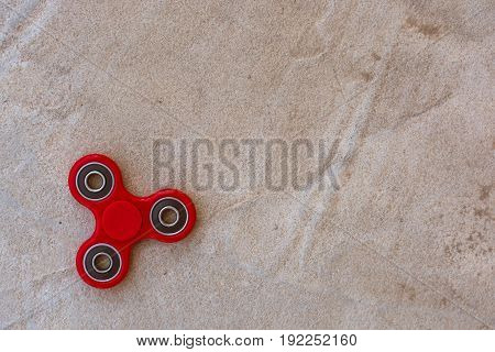 Red fidget spinner in motion stress relieving toy on concrete background.
