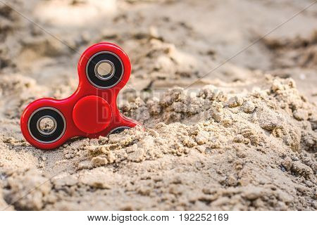 Popular red spinner gadget in 2017 against the background of sand. Modern red plastic spinner fidget game for young people.