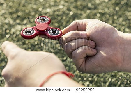 closeup of a young caucasian man playing with a red fidget spinner on nature background. Popular spinner gadget in 2017.
