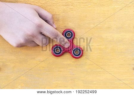 Closeup of a young caucasian man playing with a new red fidget spinner on a yellow wooden background