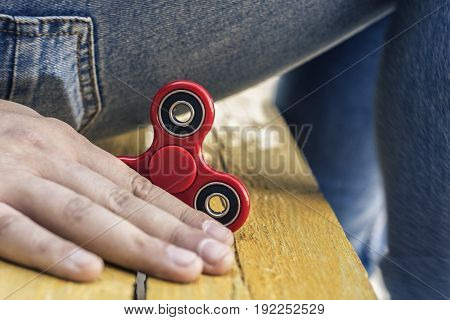 Closeup of a young caucasian man playing with a new red fidget spinner on a yellow wooden background and blue jeans