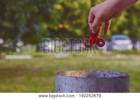 Closeup of a young caucasian man throwing a red fidget spinner in a garbage can on the background of nature.