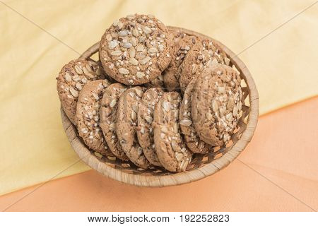 Homemade cookies with cereals in a wicker basket on a gentle pear-yellow and warm light orange background