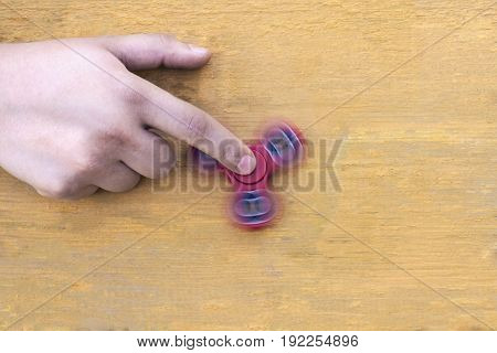 aucasian man holds his finger (hand) Red fidget spinner in motion stress relieving toy on on a yellow wooden background