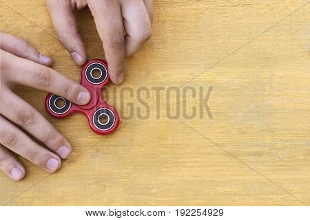 Caucasian man holds his finger (hand) Red fidget spinner in motion stress relieving toy on on a yellow wooden background
