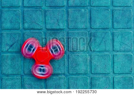 Red fidget on the blue-green background. Popular spinner gadget in 2017.