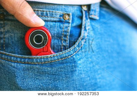Caucasian man hides his red finger fidget spinner at jeans pocket. Popular spinner gadget in 2017.
